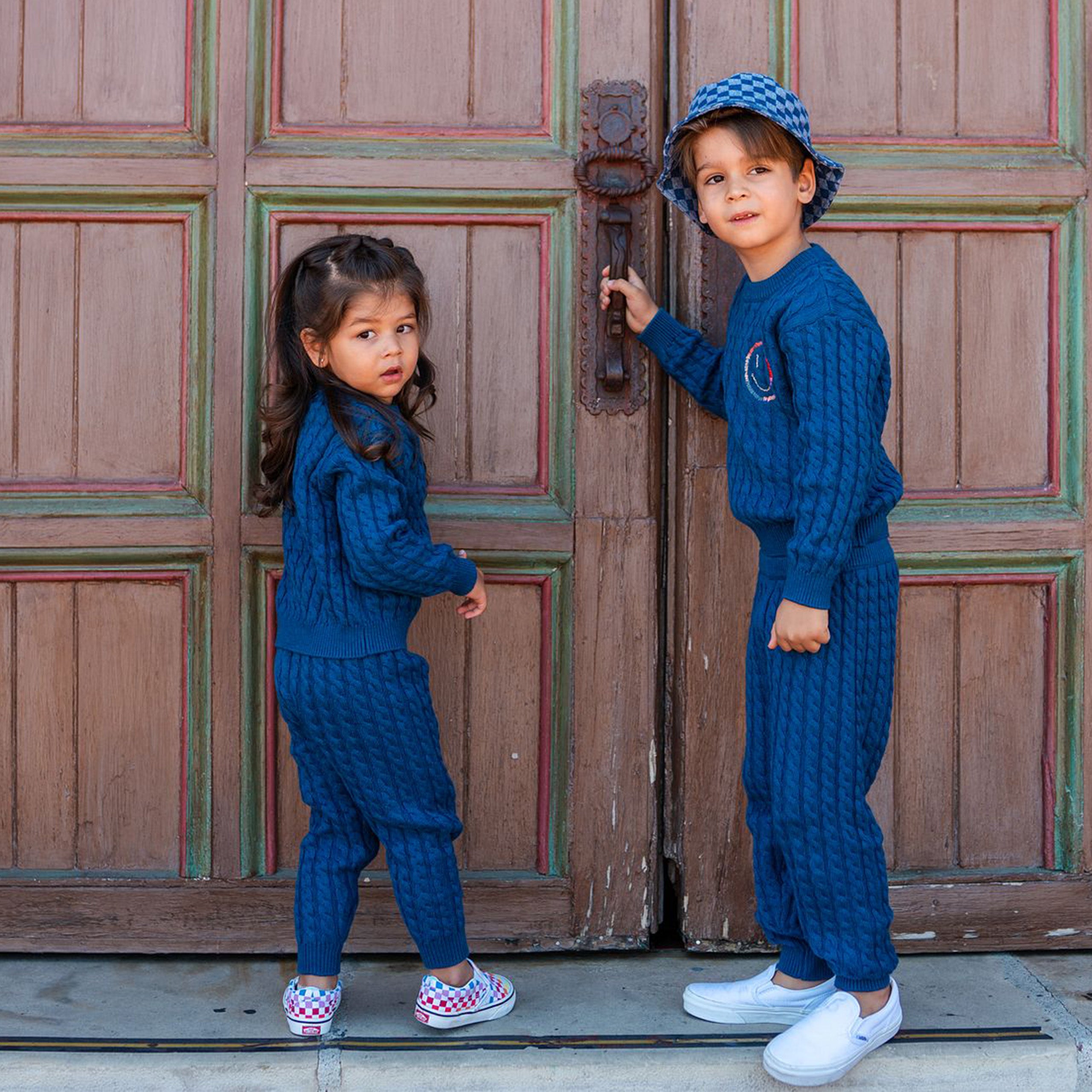 Girl and boy wearing happy cable knit sweater and pants set. 